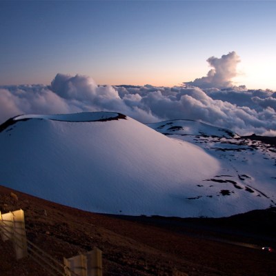 a group of clouds in the sky over a snow covered mountain