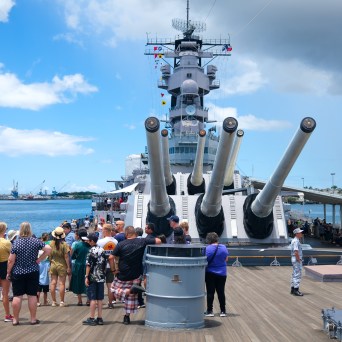 a group of people standing in front of a large ship in the background with USS Missouri (BB-63) in the background