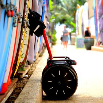 Colorful surfboards lined up with a red Segway leaning against one in a sunny outdoor area.