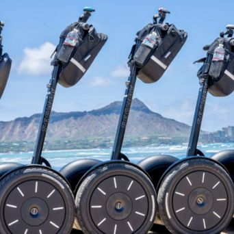 Five Segways parked in a row with a mountain and ocean in the background.