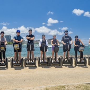 Nine people on segways lined up by a waterfront with blue skies.