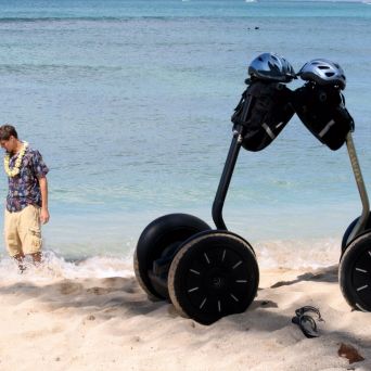 Two segways on a beach, man and woman walking by the water with leis.