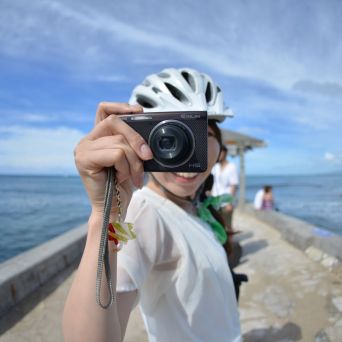 Person in helmet holding camera by the ocean on a sunny day.