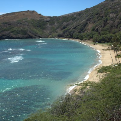 Aerial view of a curved beach with turquoise water and lush green hills.