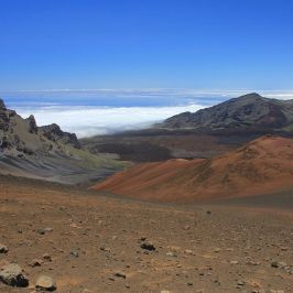 Barren volcanic landscape with rocky hills and distant mountains under a clear blue sky.