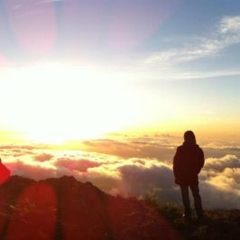 Silhouette of a person standing on a mountain at sunrise, overlooking clouds.