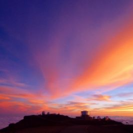 Vibrant sunset sky with pink, orange, and purple hues over silhouette buildings on a hill.
