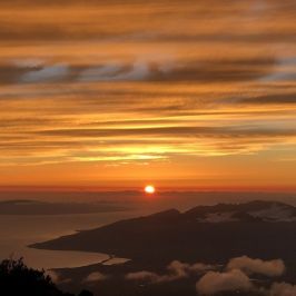 Sunrise over a mountain landscape with orange and yellow clouds.