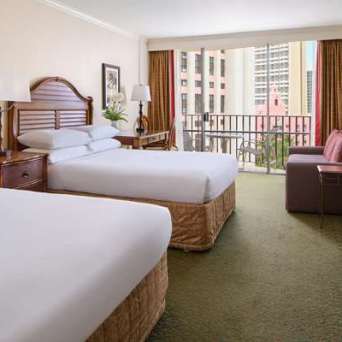 Hotel room with two beds, balcony view, and a couch beside a TV.