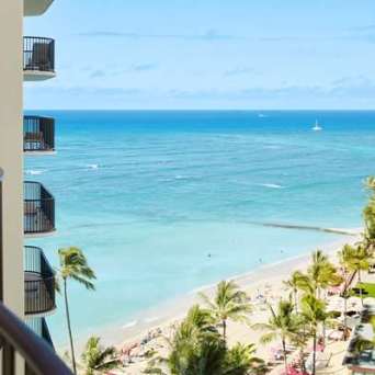 Balcony view of a tropical beach with palm trees and ocean waves.