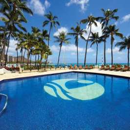 Tropical hotel pool with palm trees and ocean view in the background.