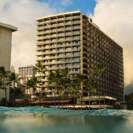 View of beachfront hotels and palm trees from ocean level at sunset.