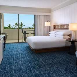 Modern hotel room with double bed, TV, lamps, and balcony view of palm trees.