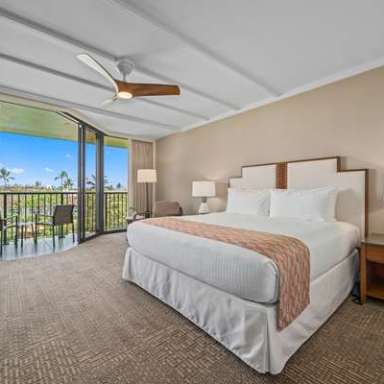 Spacious hotel room with large bed, balcony view, and modern furnishings.