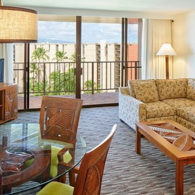 Tropical-themed living room with balcony, sofa, TV, and glass table.