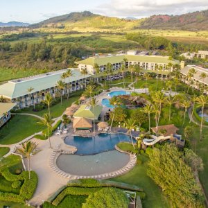 Aerial view of a resort with pools surrounded by green landscape and mountains.