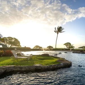 Outdoor pool with lounge chairs, palm trees, and sunset sky.