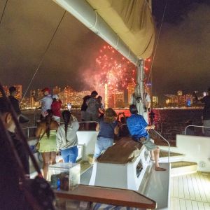 People on a boat watching fireworks over a city skyline at night.