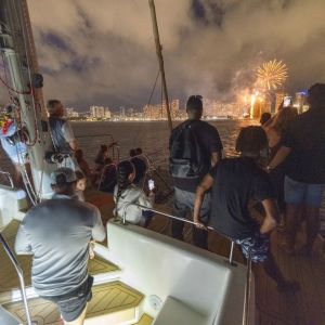 People on a boat watching city fireworks at night.