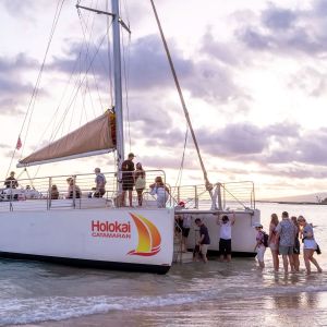 People boarding a catamaran at a beach during sunset.