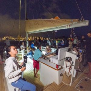 People on a sailboat at night with city lights in the background.