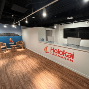 Office lobby with wood floor, two chairs, a round table, and 'Holokai Catamaran' logo on counter.