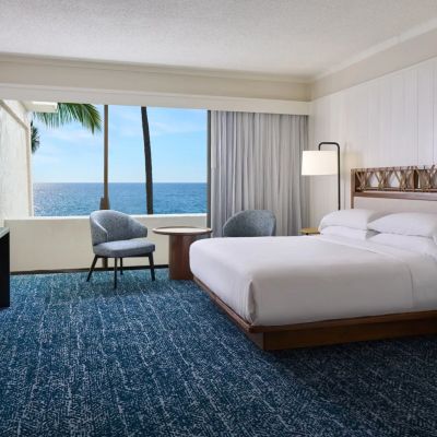 Hotel room with ocean view, double bed, seating area, and large window.