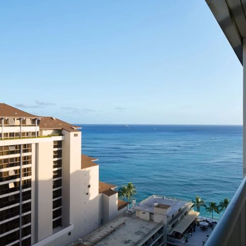 Ocean view from a high balcony with buildings and palm trees.