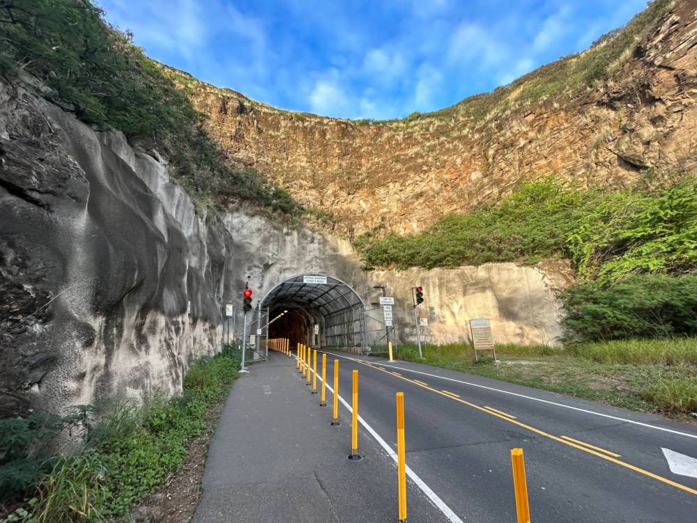 Road entering a tunnel through rocky terrain with blue sky above.