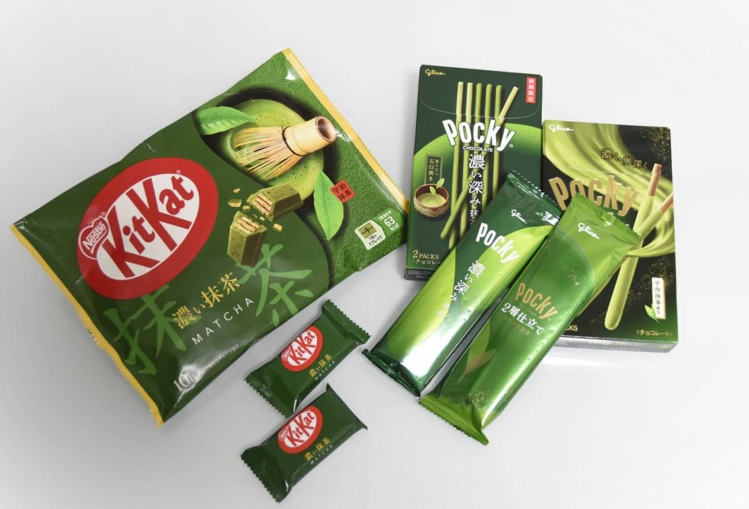 Variety of Japanese green tea snacks, including KitKat and Pocky, on a white surface.