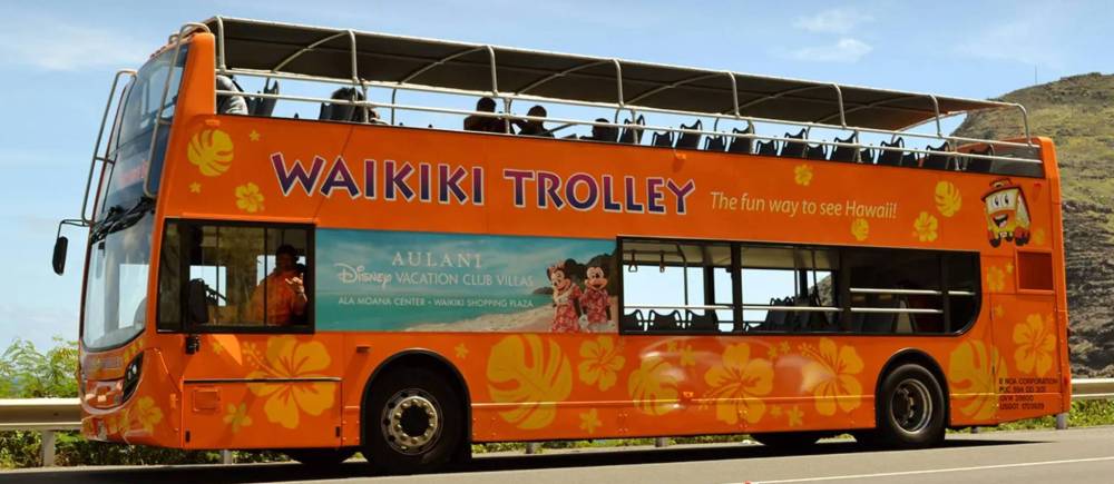 Orange double-decker tour bus with open top, labeled 'Waikiki Trolley'.