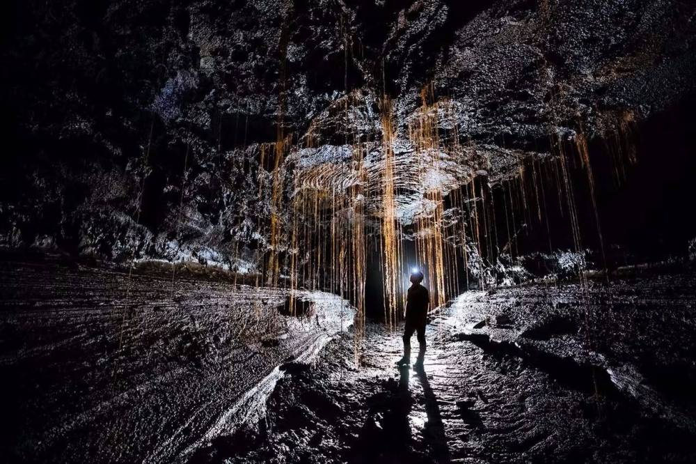 Person exploring a dark cave with hanging formations, light illuminating the path.