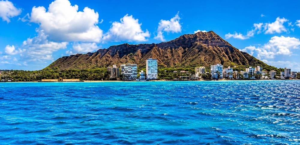 Ocean view of Diamond Head in Hawaii under a bright blue sky with scattered clouds.