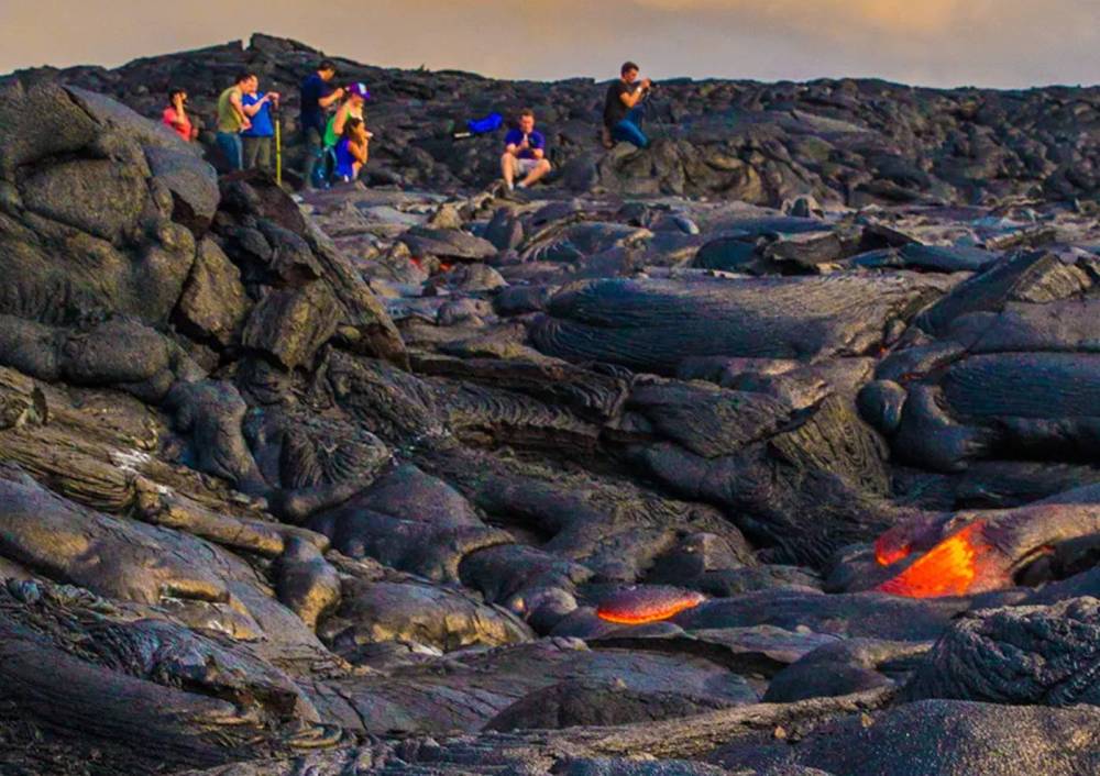 People standing on rocky terrain near flowing lava.