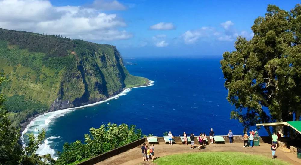 People viewing a coastal cliff and ocean under a blue sky.